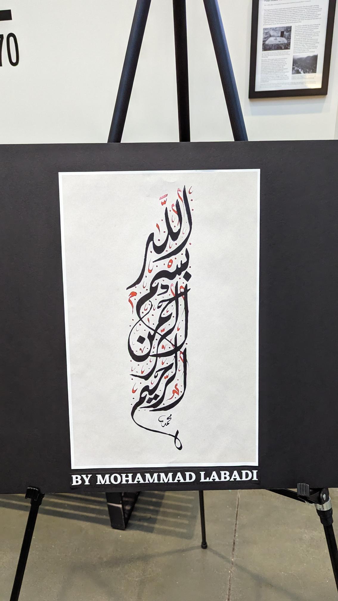 Framed Basmala piece displayed on an easel at an exhibition