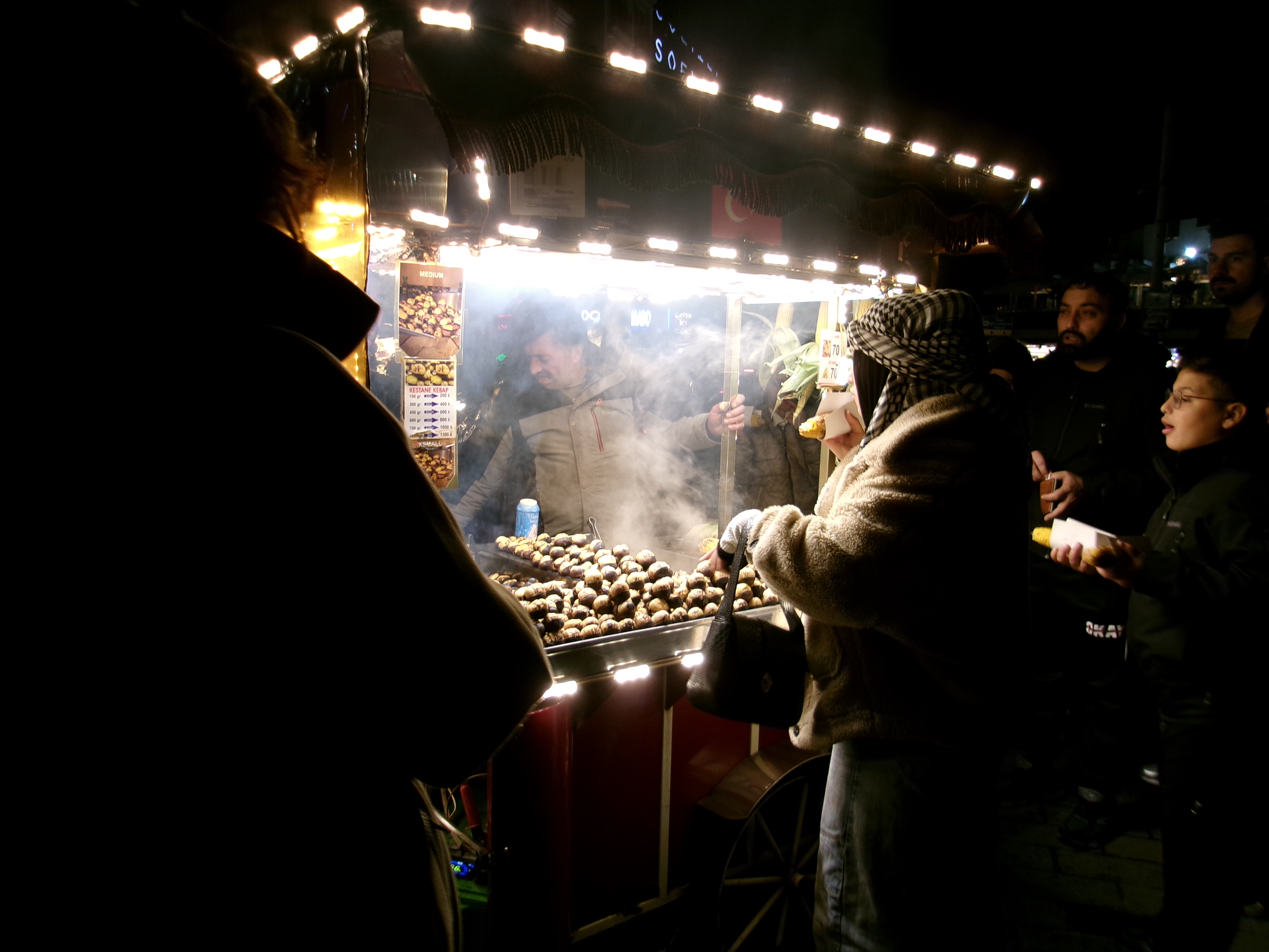 Street cart selling roasted chestnuts and corn at night, steam rising under LED lights