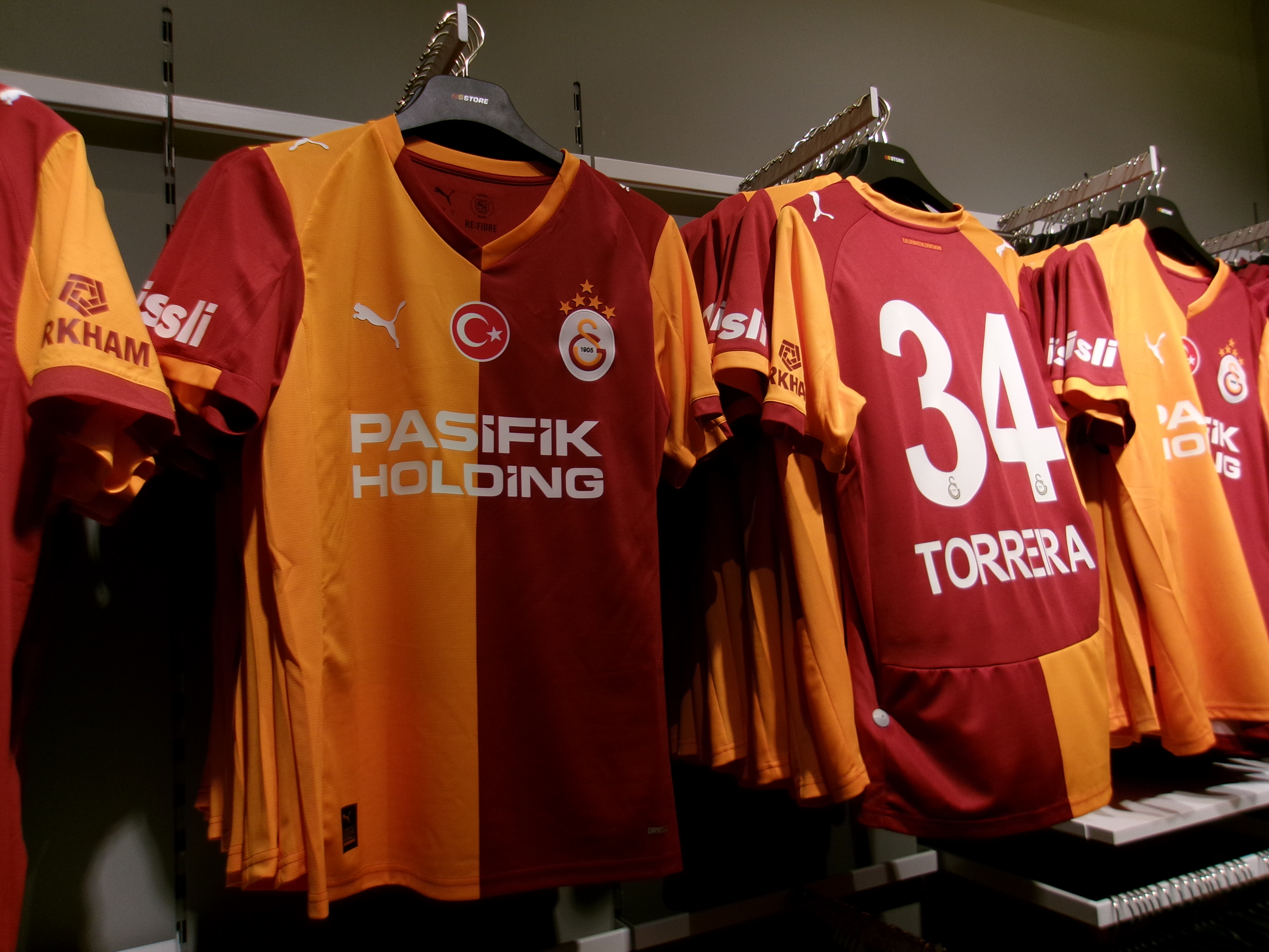 Galatasaray home jerseys hanging in a store, half yellow and half red with Torrera 34 on the back