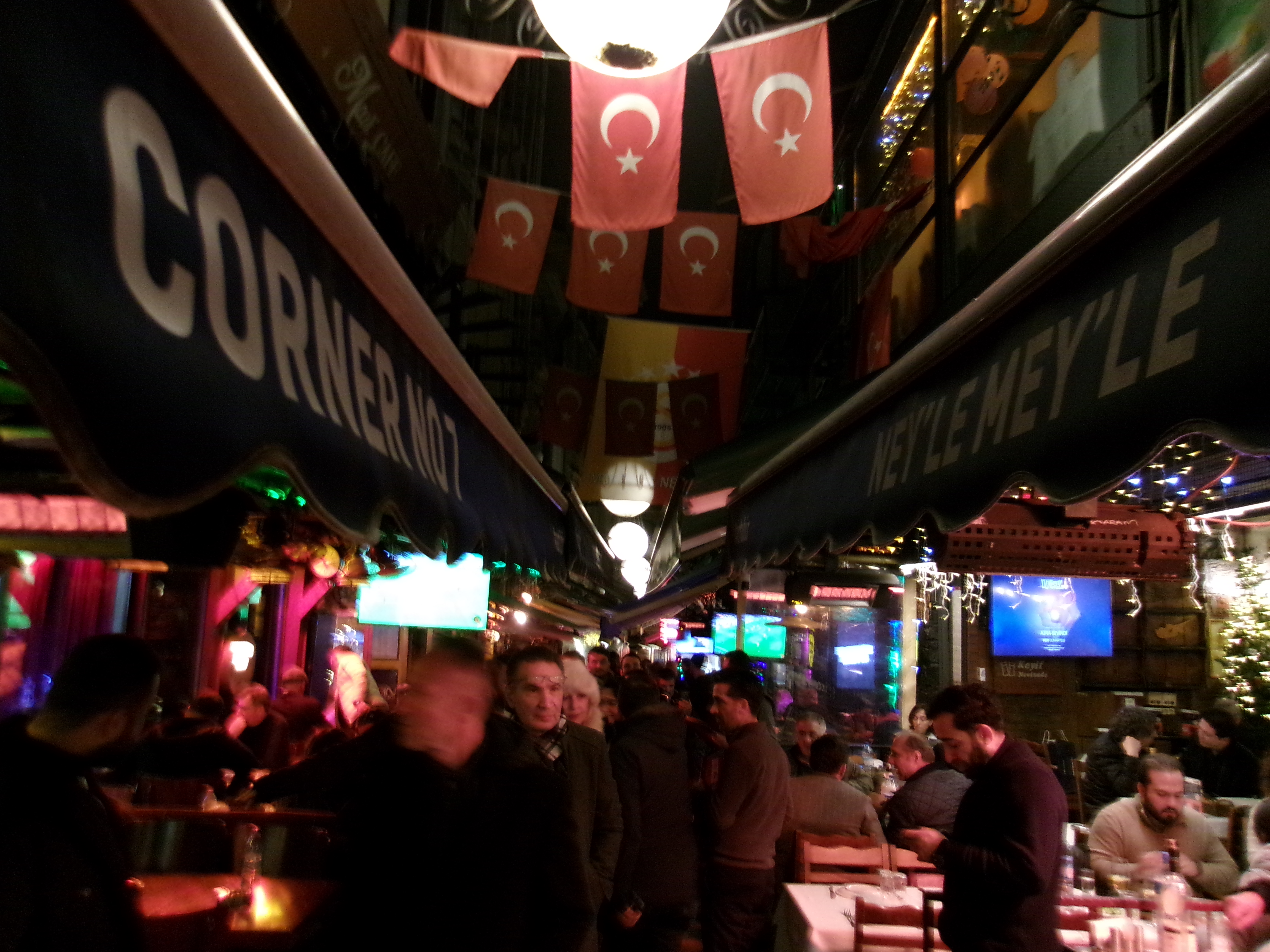 Crowded outdoor dining alley at night under Turkish flags and globe lights